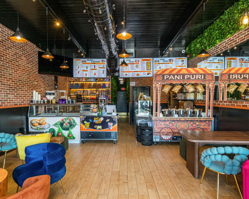Interior of a vibrant Indian restaurant with brick walls, colorful seating, and Pani Puri food stalls.