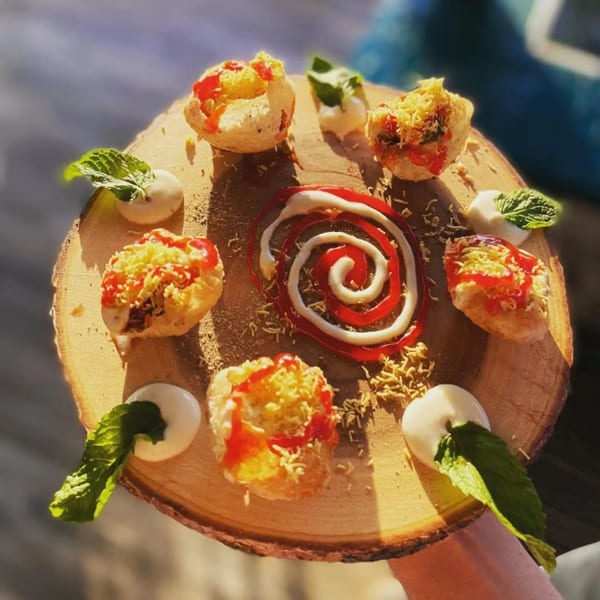 Round wooden board with six pani puri, garnished with sauce, cheese, and mint leaves.