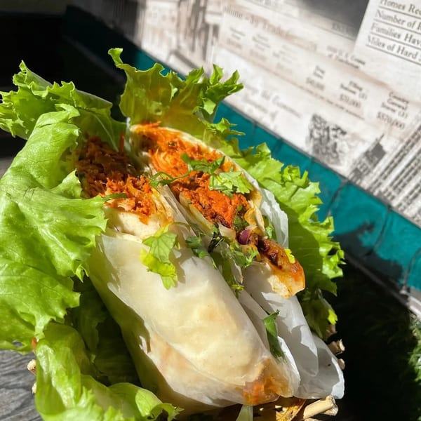 Two fresh spring rolls with orange filling and cilantro, nestled in lettuce leaves.