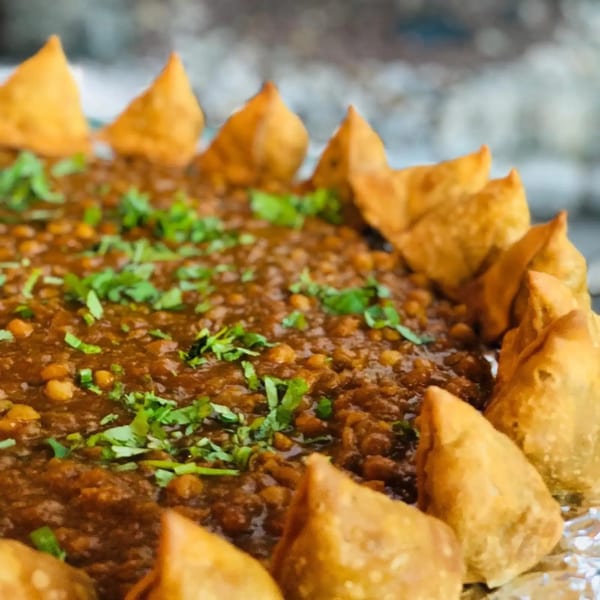 A close-up of samosas arranged around a dish of chana masala, garnished with cilantro.